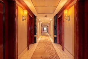 A hotel hallway with wooden doors, a patterned carpet, and wall sconces.
