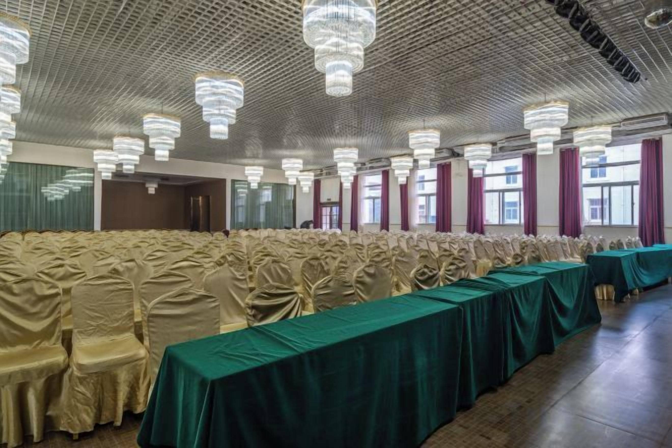 Un salón de banquetes con filas de sillas cubiertas con tela color beige, una larga mesa con mantel verde y varios candelabros.