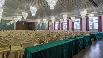 A banquet hall with rows of chairs covered in beige, a long table with a green tablecloth, and multiple chandeliers.