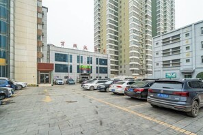 A parking lot with multiple cars, a building with a sign, and tall residential buildings in the background. - Zhoukou Hotel (Zhoukou Wanshunda Department Store) (Zhoukou)
