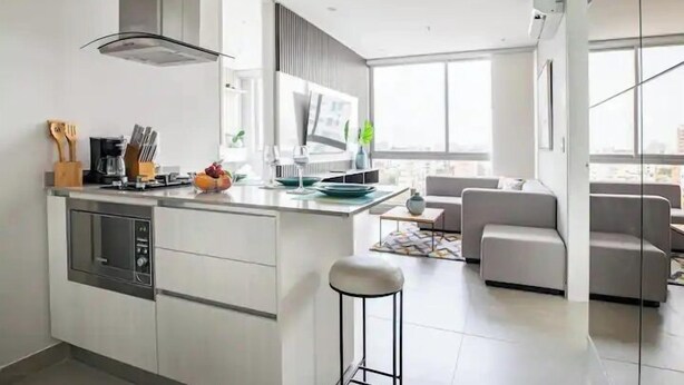 A modern kitchen with a central island, built-in appliances, and a dining area with a sofa and a coffee table. - Distrito 90 By Hostpro (Barranquilla)