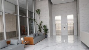 A spacious lobby with a modern grey sofa, a wooden coffee table, and potted plants. - Distrito 90 By Hostpro (Barranquilla)