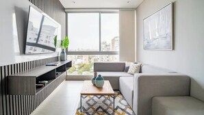 A modern living room with a large window, a flat-screen TV, a grey sofa, and a coffee table. - Distrito 90 By Hostpro (Barranquilla)