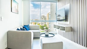A modern living room with a large window, a sofa, a coffee table, and a mounted TV. - Distrito 90 By Hostpro (Barranquilla)