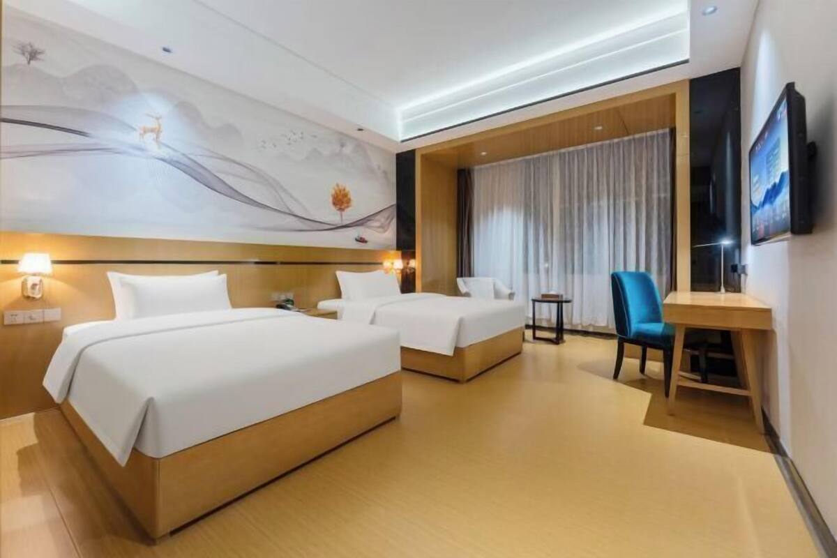 A hotel room with two beds, a desk, a chair, a TV, and a mural on the wall.