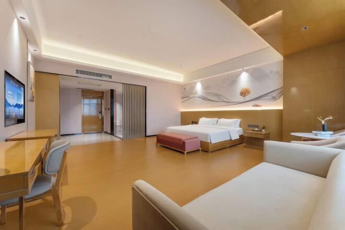 A modern hotel room with a bed, a sofa, a desk, and a TV.