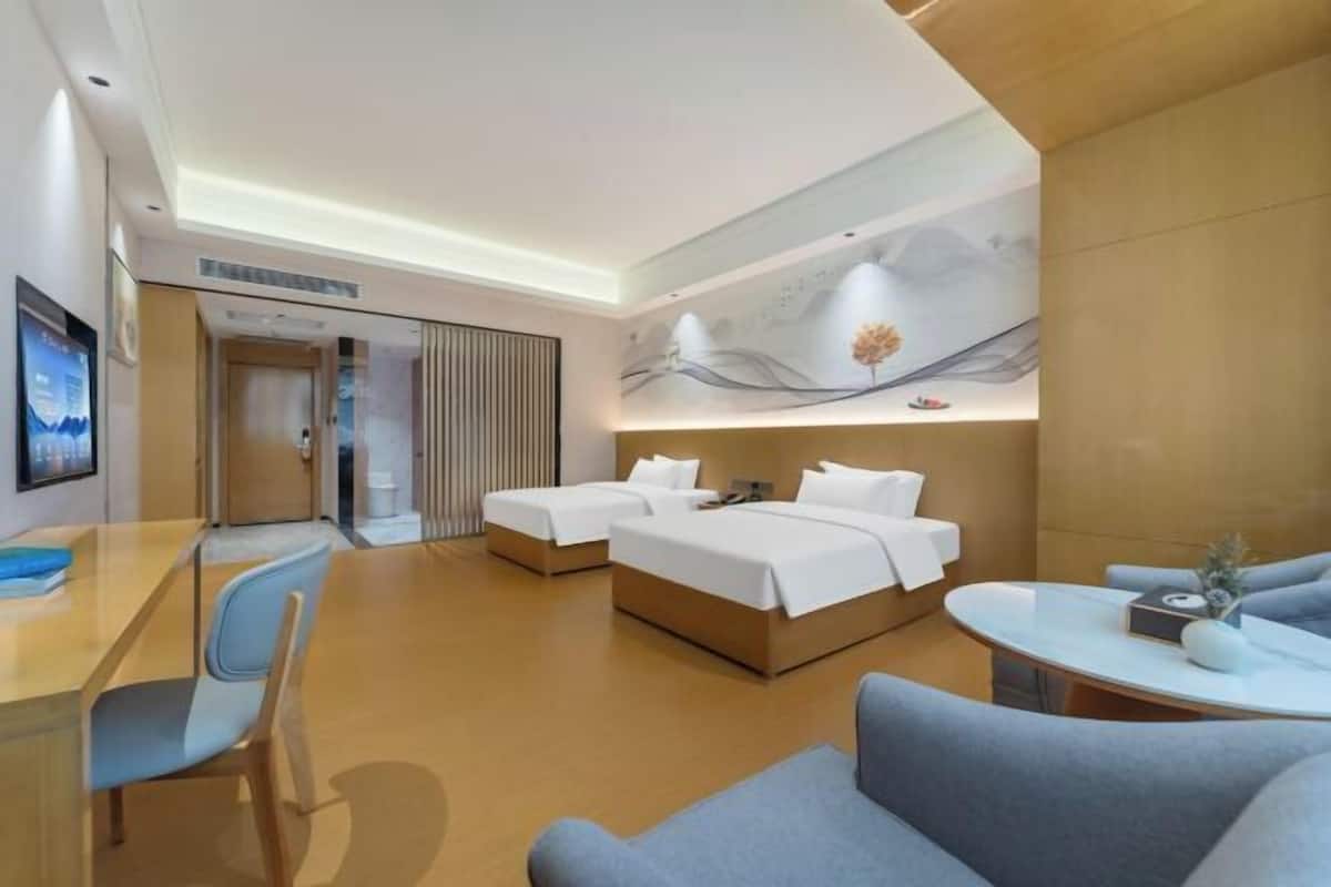 A hotel room with a bed, a desk, a chair, a sofa, and a wall with a painting.