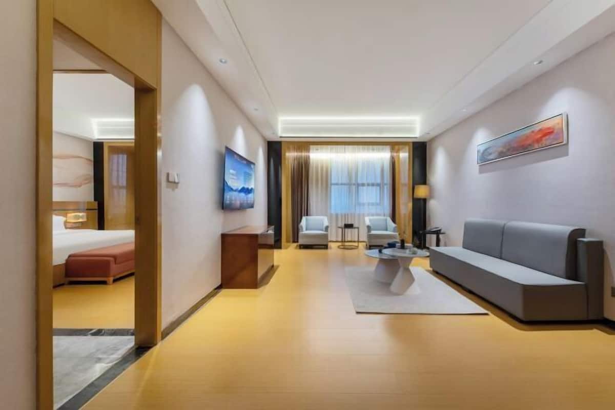 A modern hotel room with a bed, a sofa, a coffee table, and a TV.