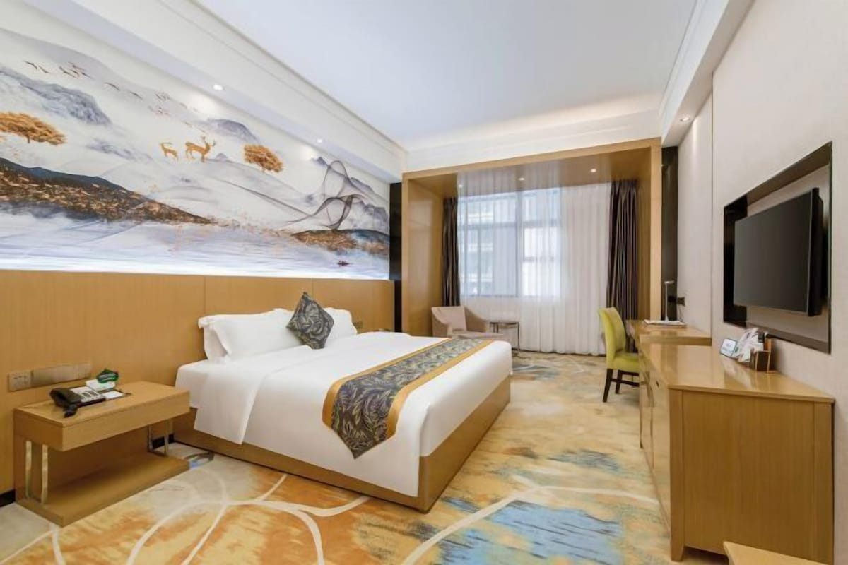 A hotel room with a large bed, a desk, a chair, a television, and a mural on the wall.