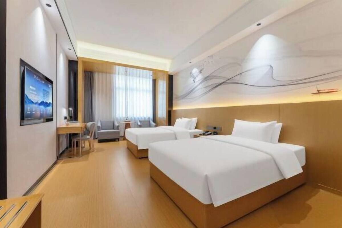 A hotel room with two beds, a desk, a chair, a TV, and a large abstract wall art piece.