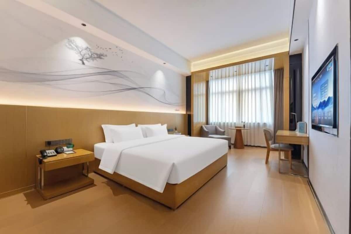 A modern hotel room with a large bed, bedside tables, a desk, and a view of the outdoors.