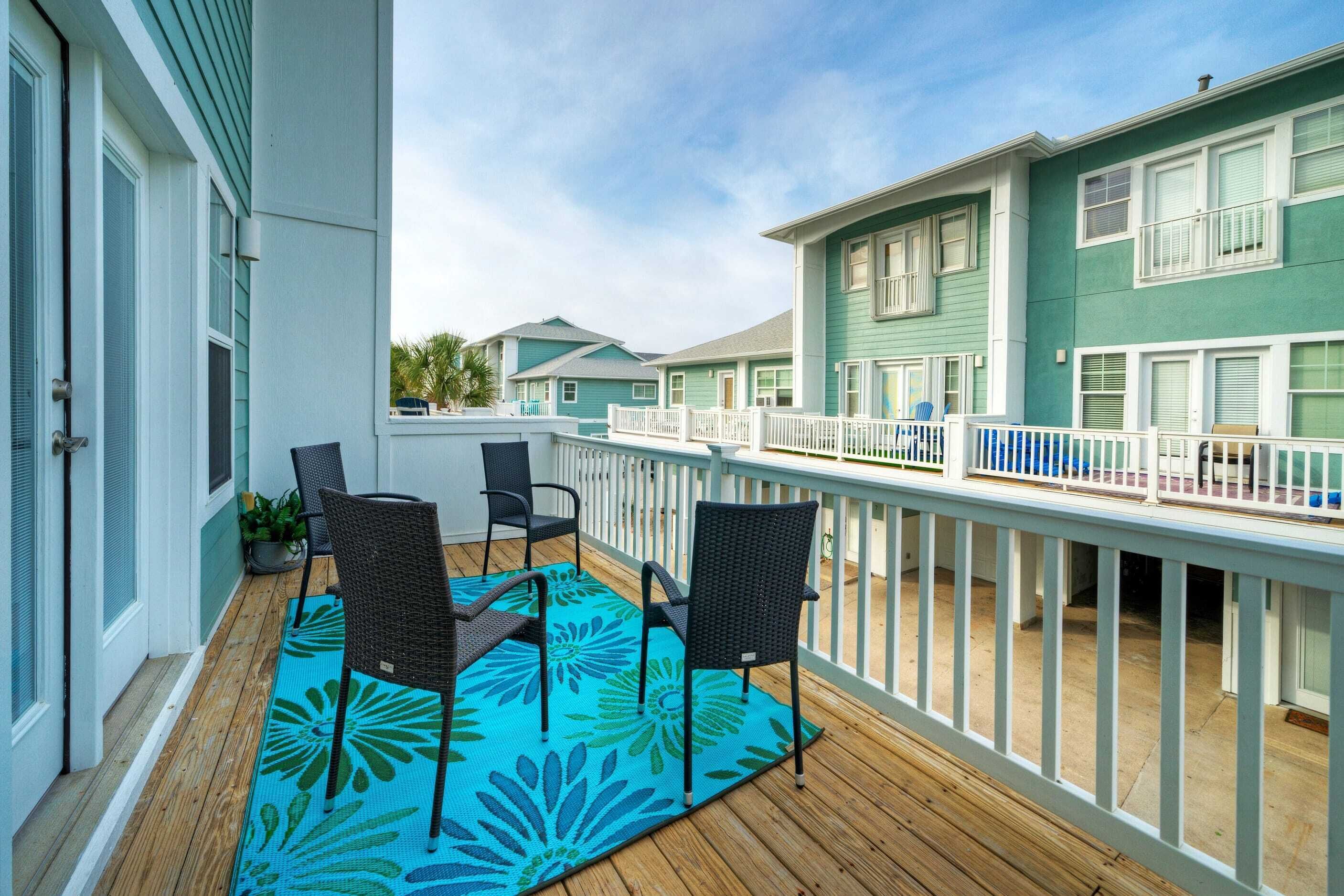 A balcony with a blue floral rug, two wicker chairs, and a white railing.