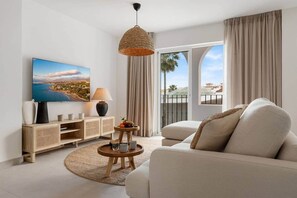 A modern living room with a sofa, a coffee table with fruit, a lamp, and a TV displaying a scenic view. - Villa Violeta Estepona Old Town (Estepona)