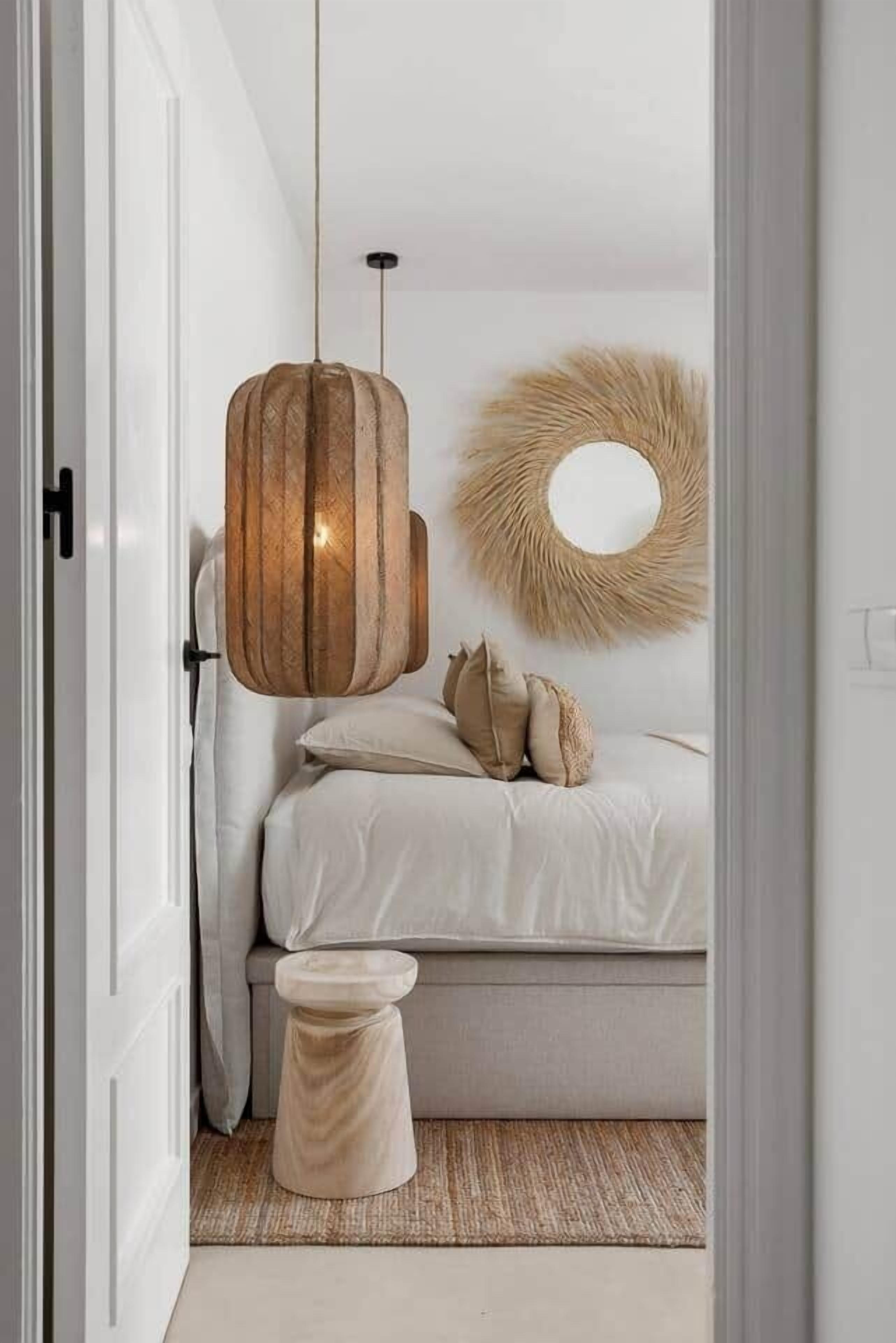 Een slaapkamer met een bed, een ronde spiegel, een hanglamp en een klein krukje.
