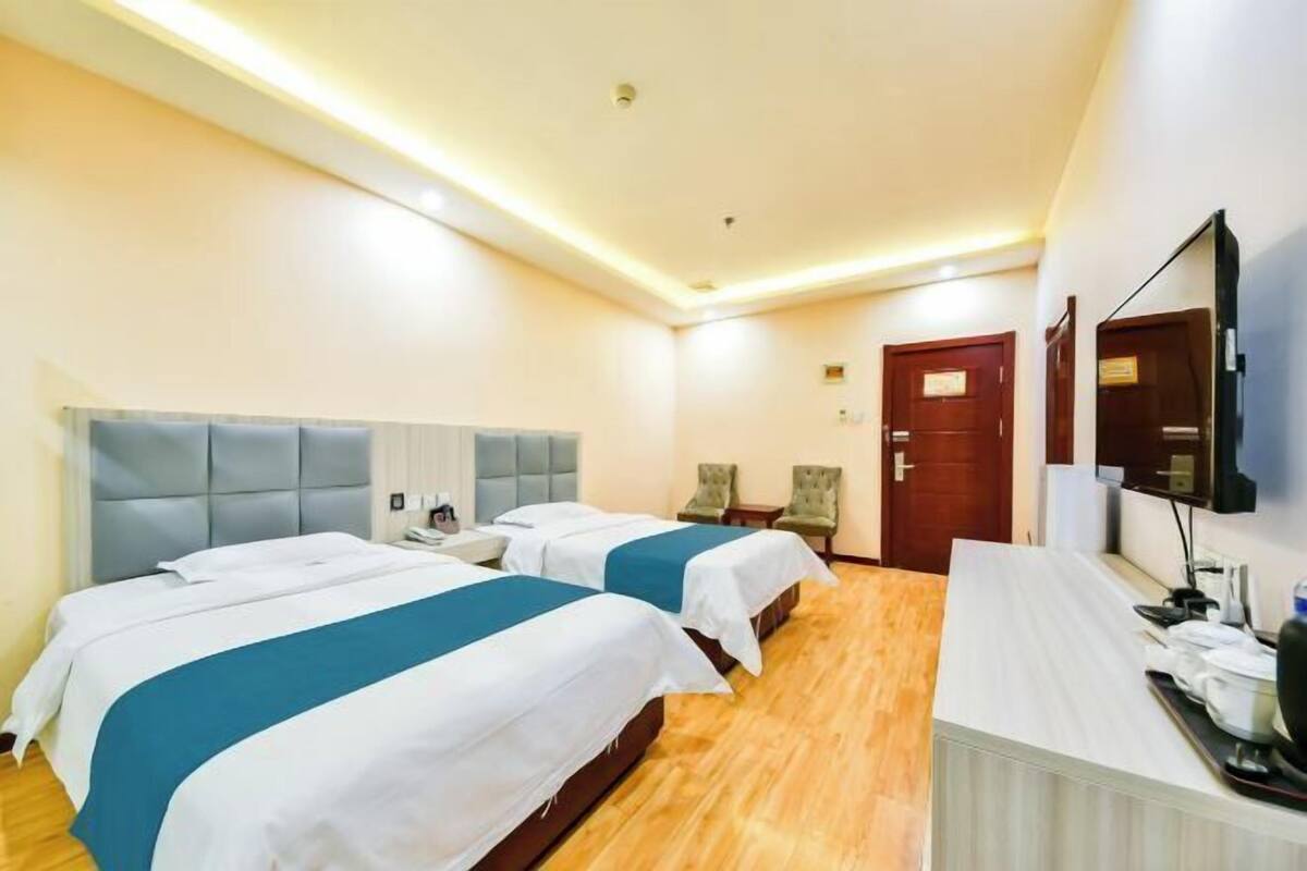 Ett hotellrum med två sängar, ett skrivbord, en stol, en TV och en dörr.