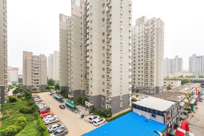 A high-rise residential building with multiple balconies, a parking area, and a blue-roofed structure.