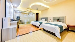 Une chambre d’hôtel avec deux lits, un bureau et une salle de bain séparée par une paroi en verre.