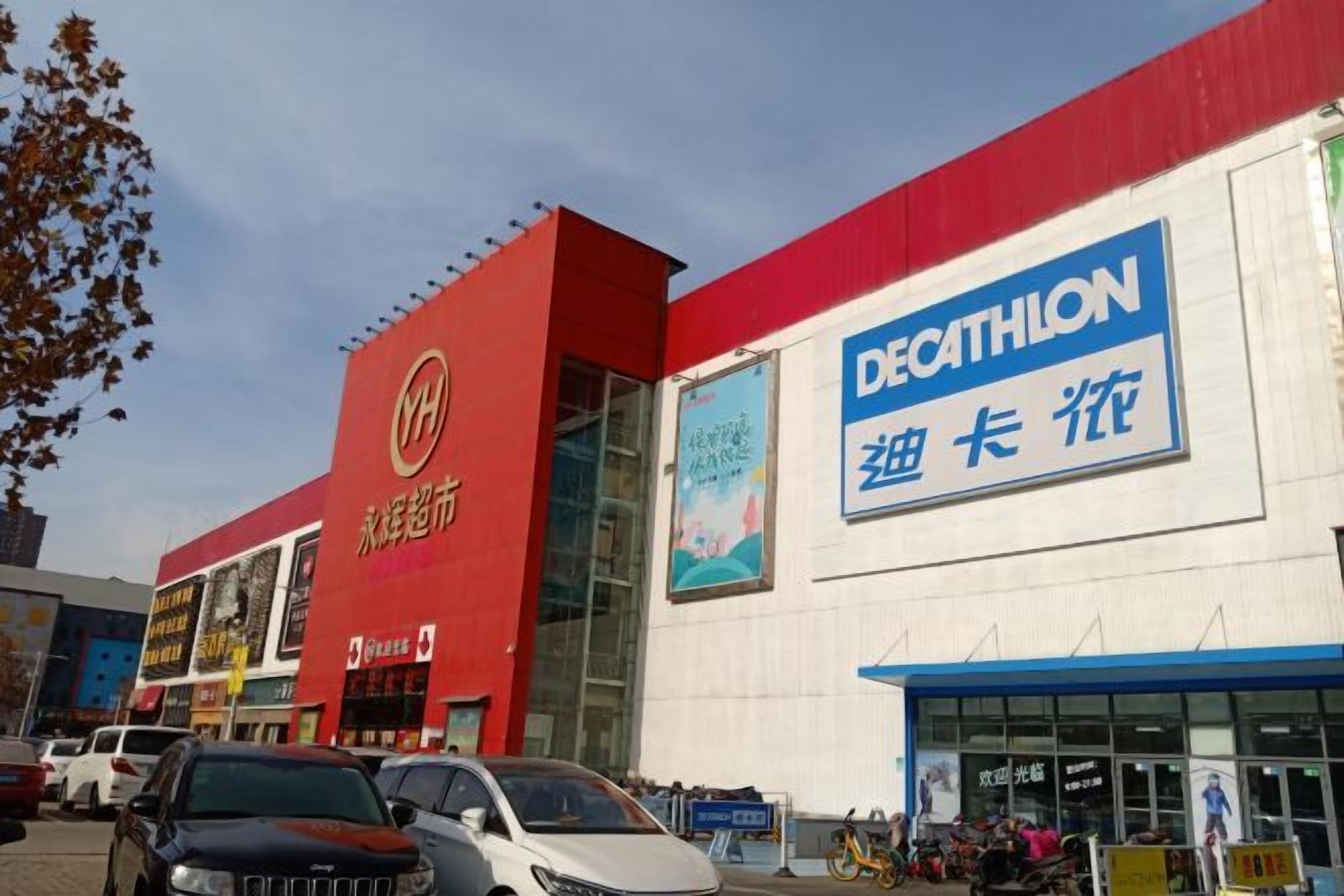 A building with a red and white facade, a large blue sign reading 'DECATHLON,' and multiple cars parked in front.