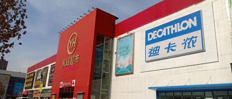 A building with a red and white facade, a large blue sign reading 'DECATHLON,' and multiple cars parked in front.