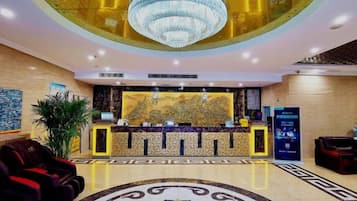 A hotel lobby with a reception desk, a large chandelier, and a decorative floor pattern.