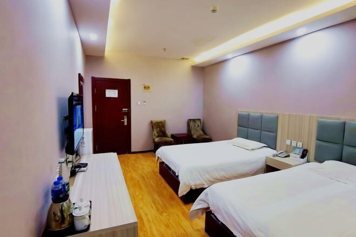 A hotel room with two beds, a desk, a chair, a TV, and a door.
