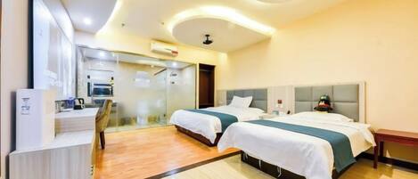 A hotel room with two beds, a desk, a mirror, and a bathroom visible through a glass partition.