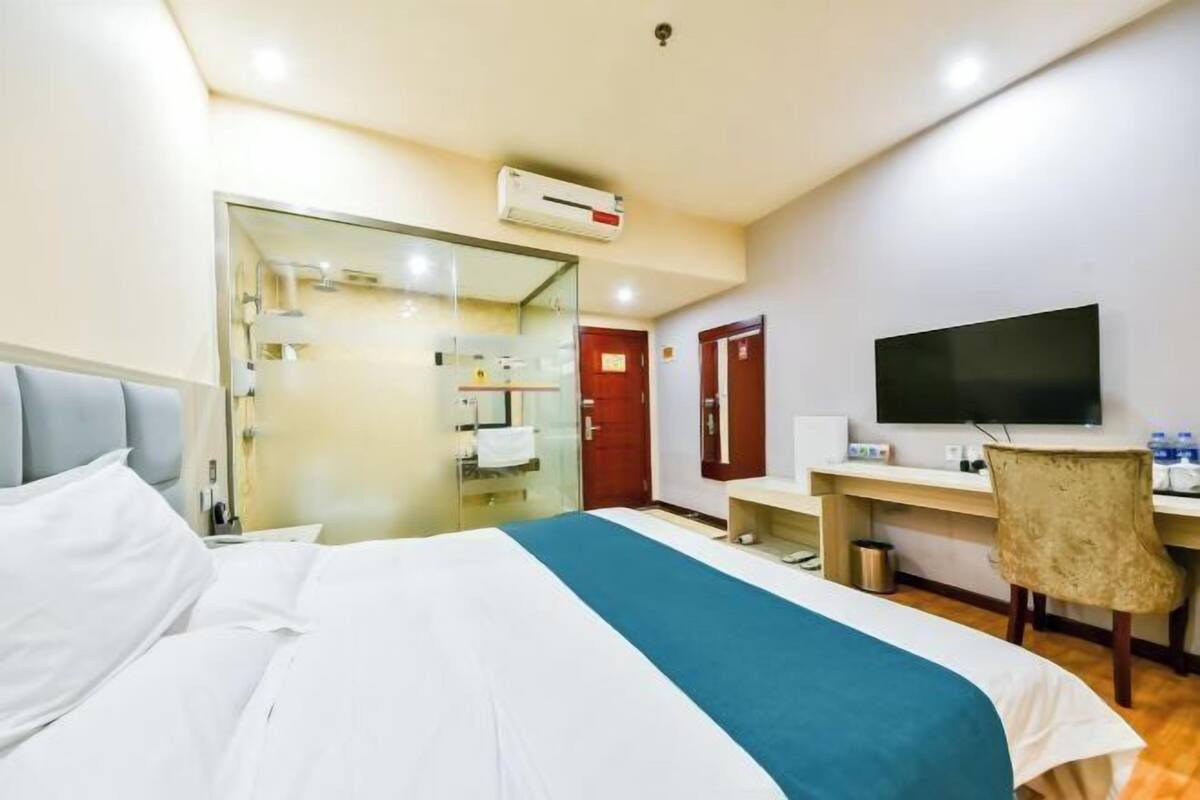 Ett hotellrum med en säng, ett skrivbord, en stol, en tv och ett badrum som syns genom en glasdörr.