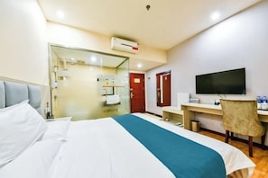A hotel room with a bed, a desk, a chair, a TV, and a bathroom visible through a glass door. - Huayi Hotel(Shijiazhuang Huai'an East Road) (Shijiazhuang)