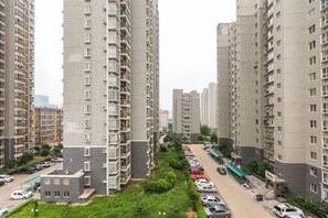 Un edificio residencial de gran altura con varios balcones, un estacionamiento y una pequeña área verde.