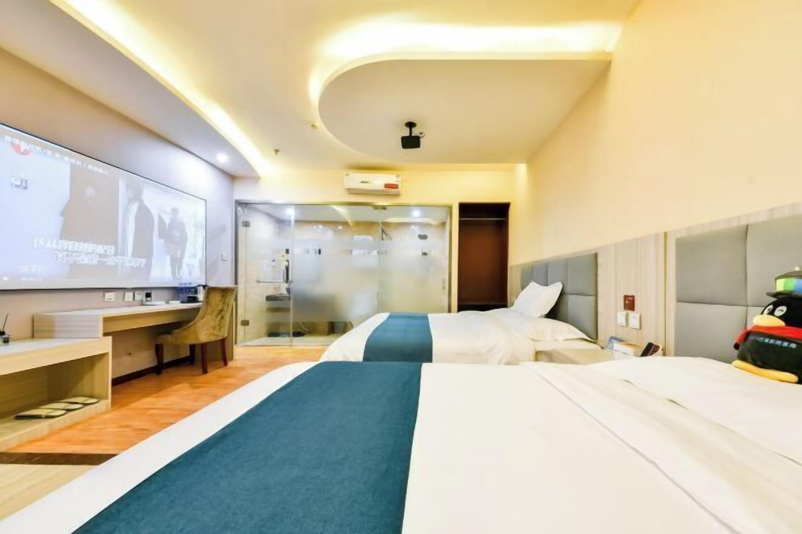 A hotel room with two beds, a desk, a TV, and a glass shower enclosure.