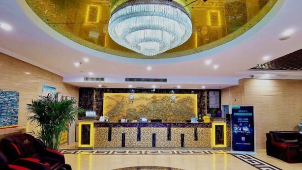 Un hall d’hôtel avec un grand lustre, un comptoir d’accueil agrémenté d’un décor, un espace salon doté d’un sol à motifs et une grande plante.