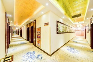 Corredor de hotel com piso de mármore, portas de madeira e obras de arte emolduradas nas paredes.