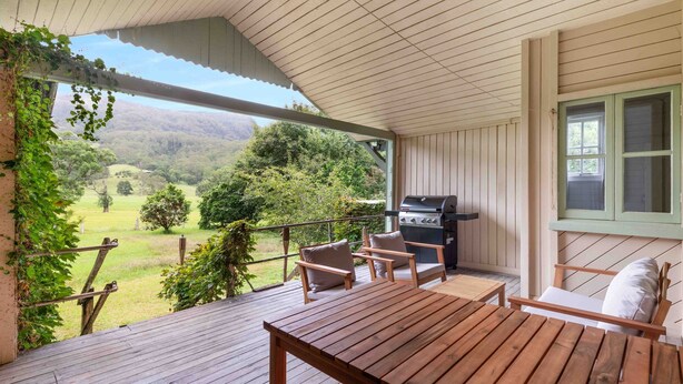 En overdækket terrasse med grill, træmøbler og udsigt over et grønt landskab.