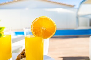 Dos vasos de jugo de naranja con una rodaja de naranja en el borde, sobre una mesa con un tazón de almendras.