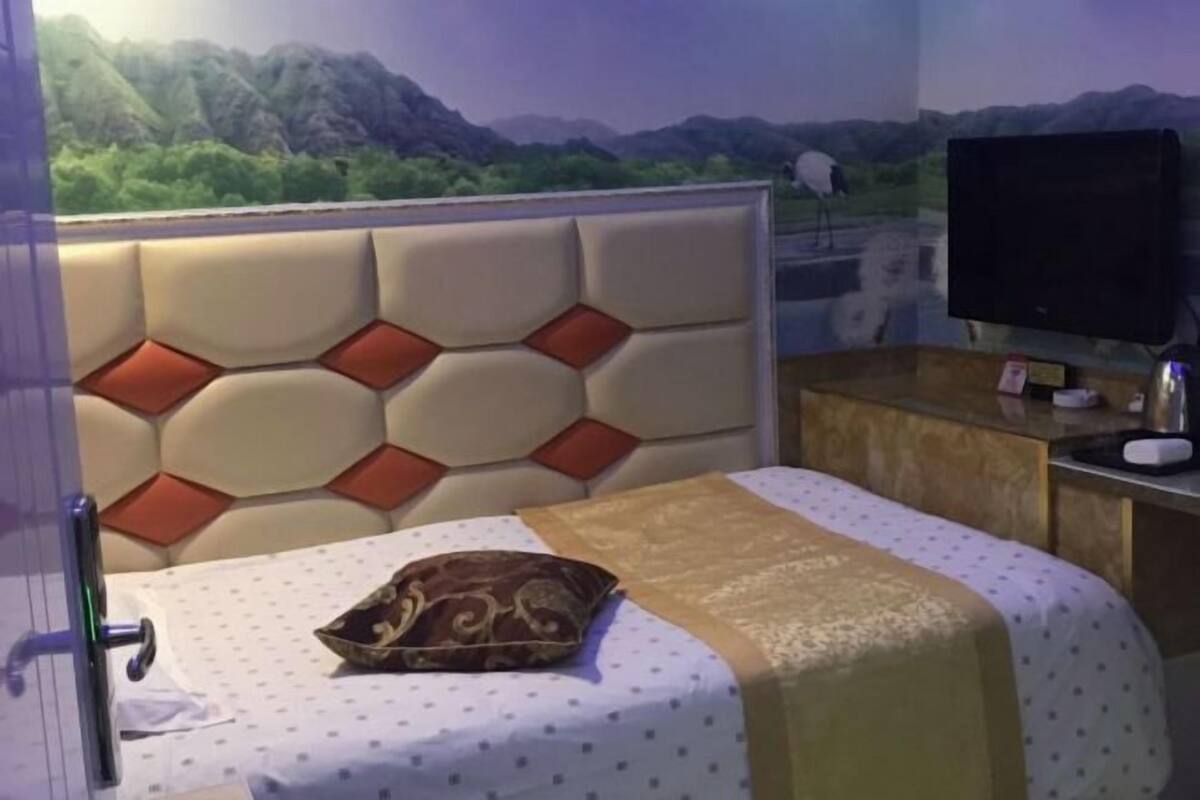 A hotel room with a bed, a television, a desk, and a view of mountains.