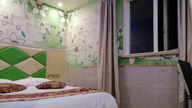 A bedroom with a bed, floral wallpaper, a window with curtains, and a green headboard. - Jinqilin Hostel (Shanghai Waigaoqiao) (Shanghai)