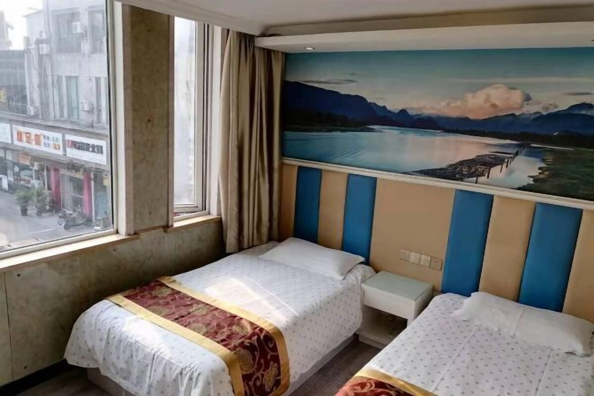 A hotel room with two beds, a window with curtains, and a mural of a lake and mountains on the wall.