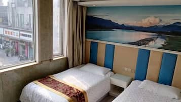 A hotel room with two beds, a window with curtains, and a mural of a lake and mountains on the wall.