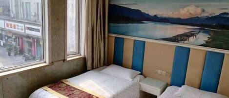 A hotel room with two beds, a window with curtains, and a mural of a lake and mountains on the wall.