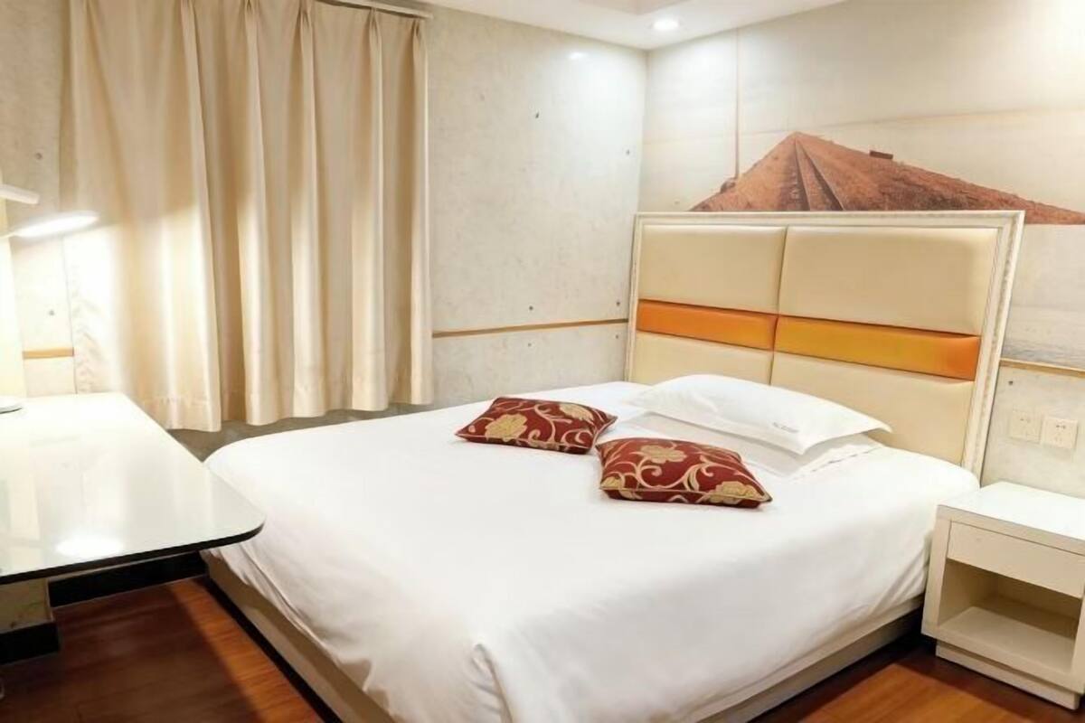 A hotel room with a bed, a nightstand, a desk, and a wall-mounted light.