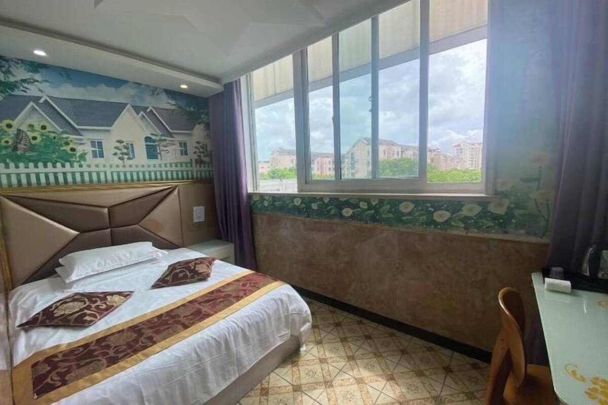 A hotel room with a bed, a window with a view, a small table, and a chair.