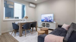 A modern living room with a sofa, a dining table with chairs, a TV, and a window. - Capitol Chill - Modern Luxury Townhouse (Seattle)