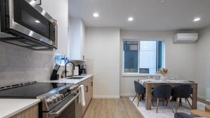 A modern kitchen with a built-in oven, microwave, and stove. There is a dining area with a table and chairs. - Capitol Chill - Modern Luxury Townhouse (Seattle)