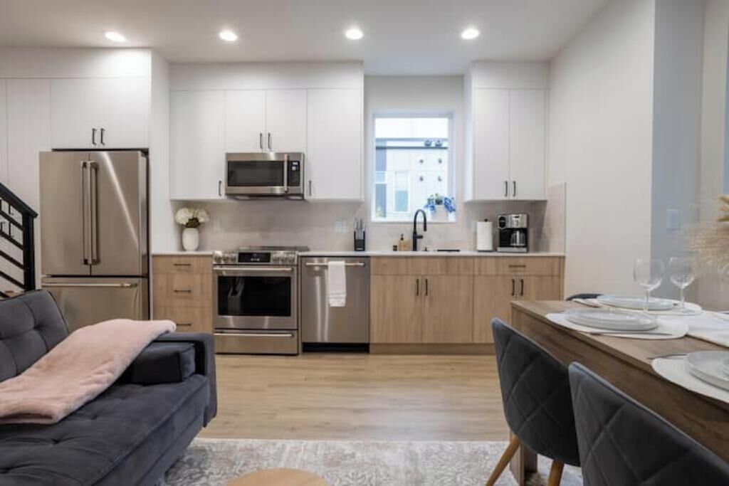 A modern kitchen with stainless steel appliances, wooden cabinets, and a dining area with a table set for two.