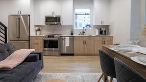 A modern kitchen with stainless steel appliances, wooden cabinets, and a dining area with a table set for two. - Capitol Chill - Modern Luxury Townhouse (Seattle)
