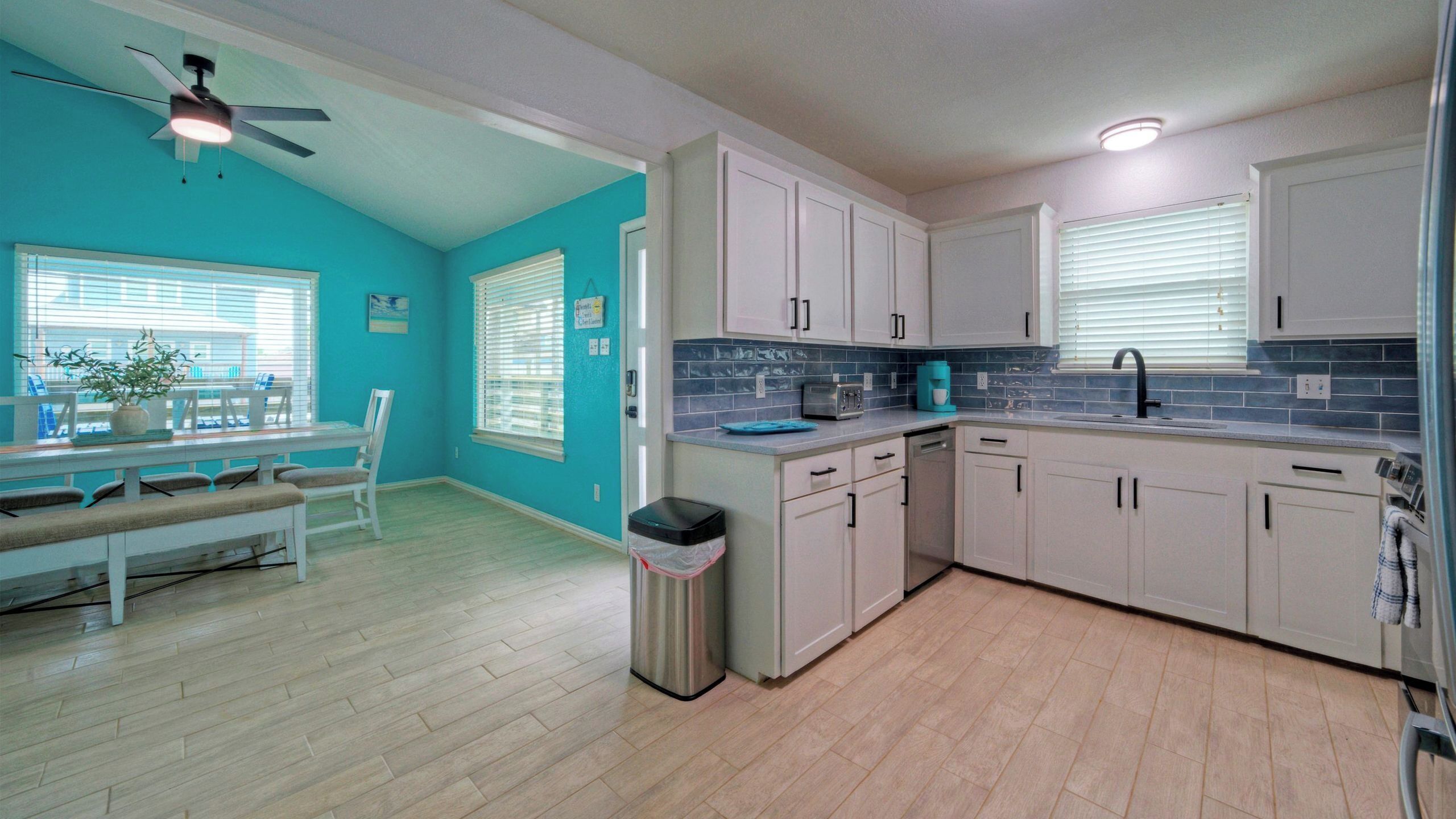 A kitchen with white cabinets, a blue backsplash, and a ceiling fan.