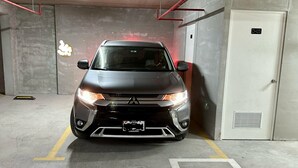 A car parked in a garage with concrete walls, a door labeled "D-03", and a ventilation system on the wall.