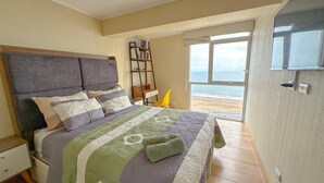 A bedroom with a bed, a nightstand, a bookshelf, and a view of the ocean.