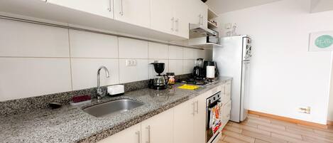 Cocina moderna con armarios blancos, encimeras de granito, un lavamanos de acero inoxidable, una cafetera y un refrigerador.