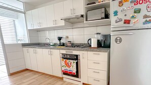 A modern kitchen with white cabinets, a built-in oven, a coffee maker, and a refrigerator adorned with stickers.